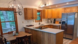 Una cocina moderna con armarios de madera, un refrigerador de acero inoxidable, una isla integrada con taburetes y un amplio ventanal con vistas a una terraza.