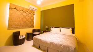 Une chambre à coucher avec un grand lit, une chaise en osier, une petite table et un climatiseur fixé au mur.