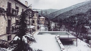 A stone building with multiple balconies and a pool area surrounded by snow-covered trees and hills. - Styga Mountain Resort (Aigialeia)