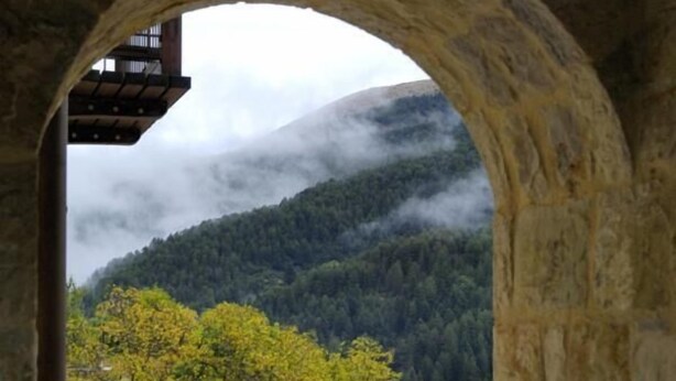 A stone archway leading to a pool area with a view of a forested mountain and a building with a balcony. - Styga Mountain Resort (Aigialeia)