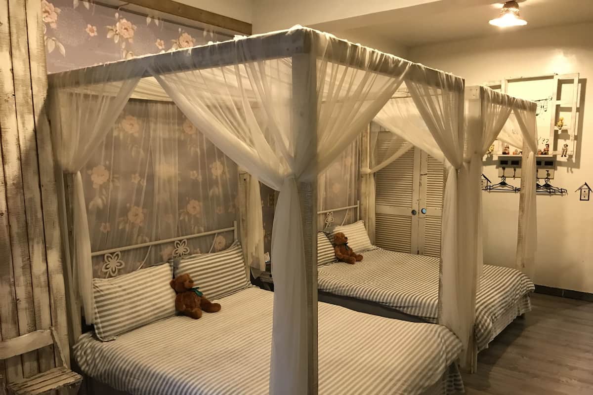 Quarto com duas camas, cada uma com dossel e cortinas de padrão floral. Há dois ursinhos de pelúcia nas camas.