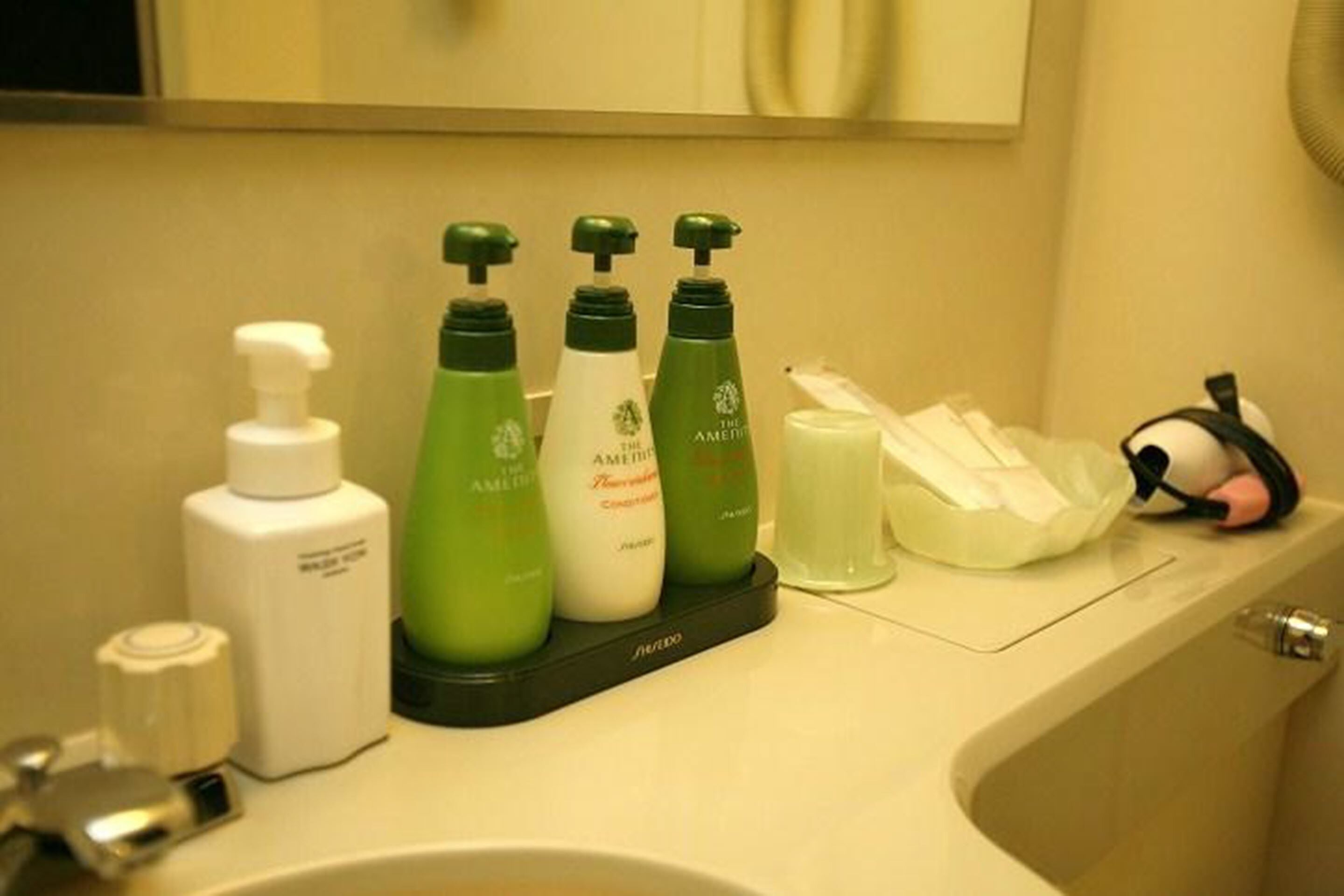 A bathroom counter with toiletries including a bottle of shampoo, a bottle of conditioner, and a bottle of lotion.