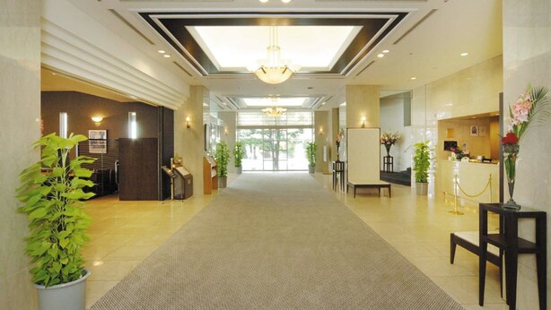 Eine Hotelhalle mit einem zentralen Kronleuchter, einer Rezeption, Topfpflanzen und einem Teppichboden.