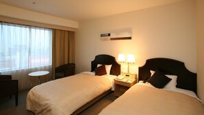 Ein Hotelzimmer mit zwei Betten, einem kleinen Tisch, einem Stuhl und einem Fenster mit Vorhängen.