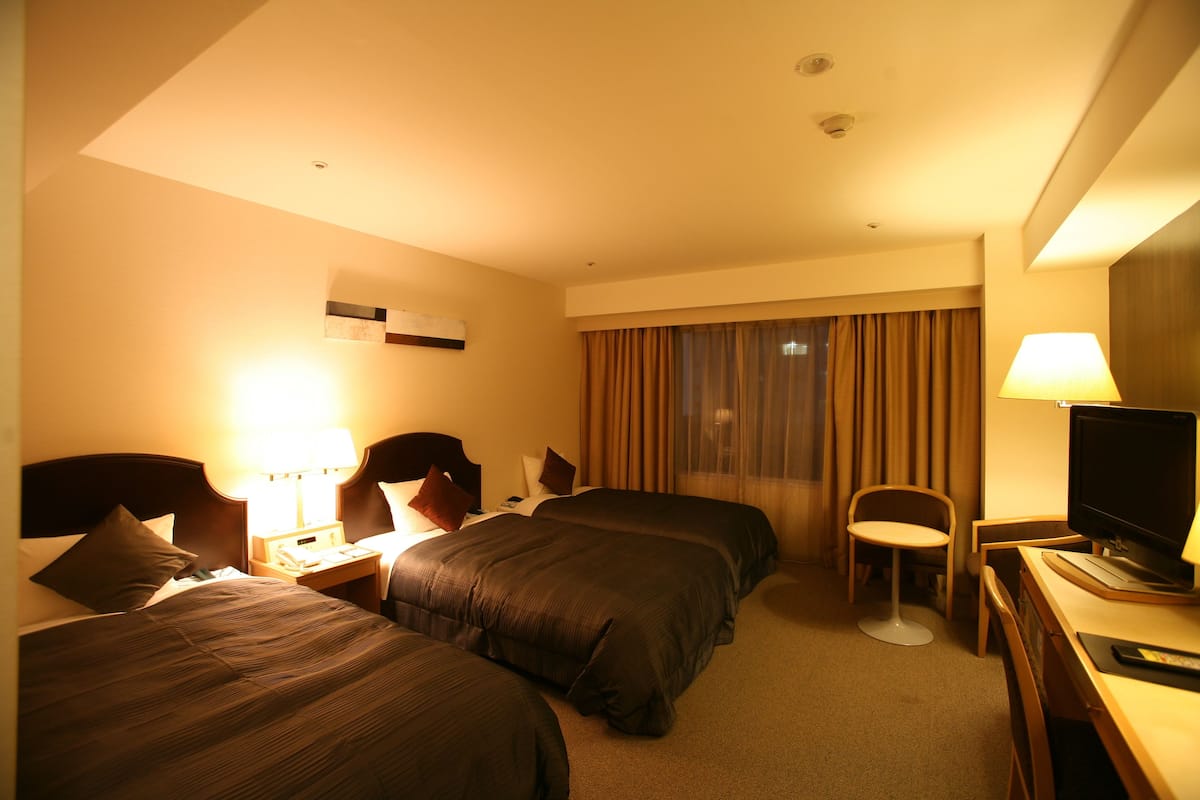 Een hotelkamer met twee bedden, een bureau met een televisie en een stoel.