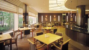 Ein großzügiges Restaurant mit mehreren Tischen und Stühlen, große Fenster mit Blick auf Grünflächen und ein modernes Decken-Design.