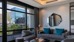 Una sala de estar moderna con un sofá gris, dos sillones, una mesa de centro y un amplio ventanal con vistas a la ciudad.