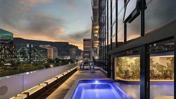 Zona de piscina en la azotea con jacuzzi, sillones de descanso y vistas a la ciudad al atardecer.