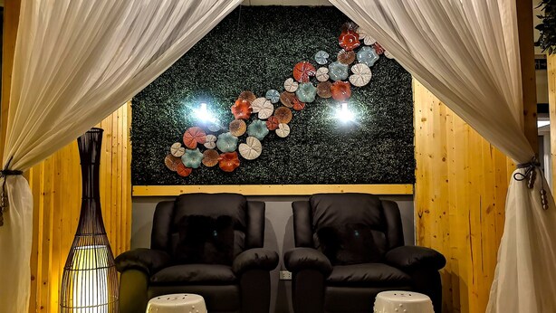 A cozy room with a black leather sofa, two white ottomans, a black and white lamp, and a wall decorated with colorful paper flowers. - Mactan Cebu Waiting Lounge (Lapu-Lapu)
