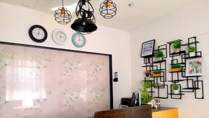 A reception desk with a wooden counter and a modern light fixture above. There are three clocks on the wall and a decorative panel with a floral pattern. - Mactan Cebu Waiting Lounge (Lapu-Lapu)