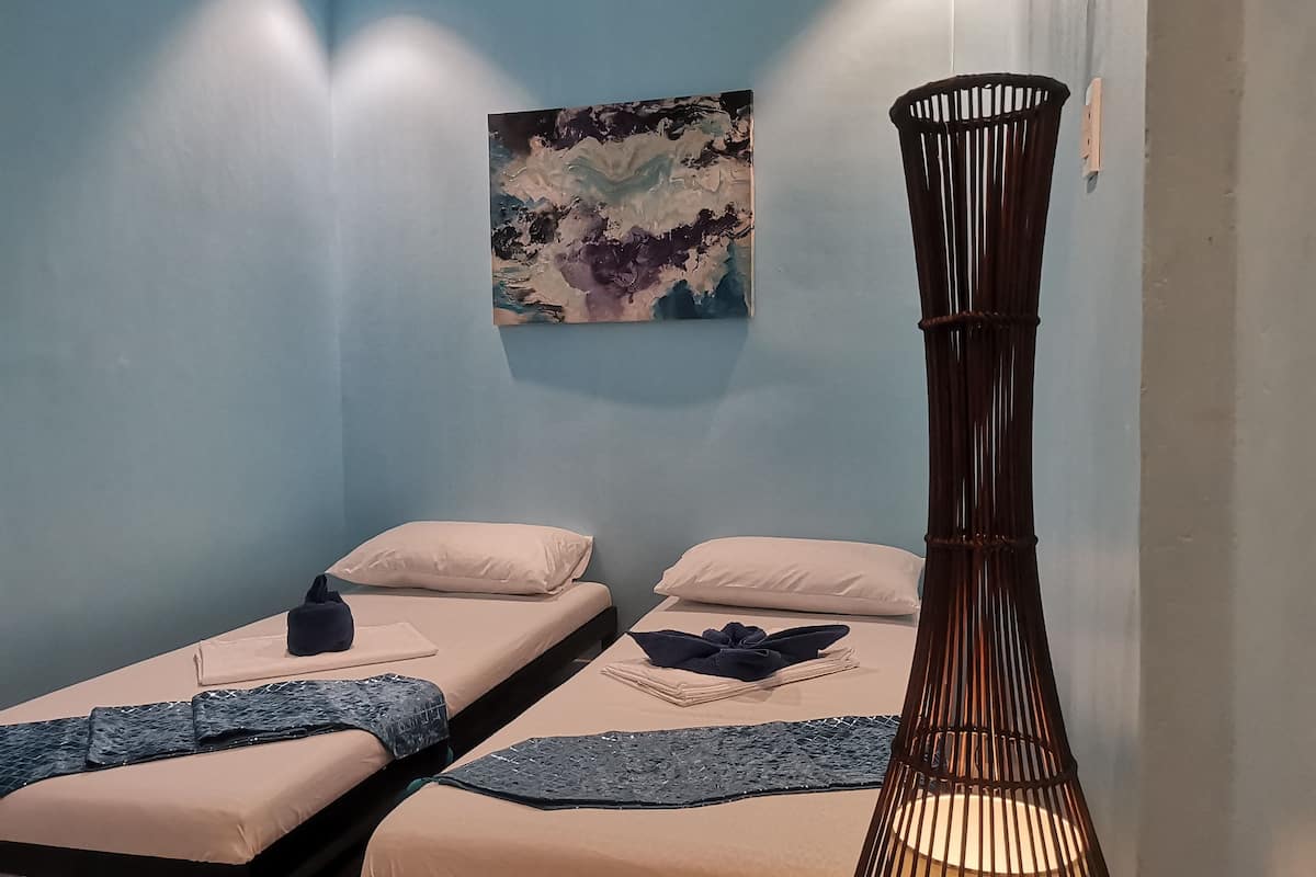 A room with two beds, a wall-mounted painting, and a tall, slender lamp.