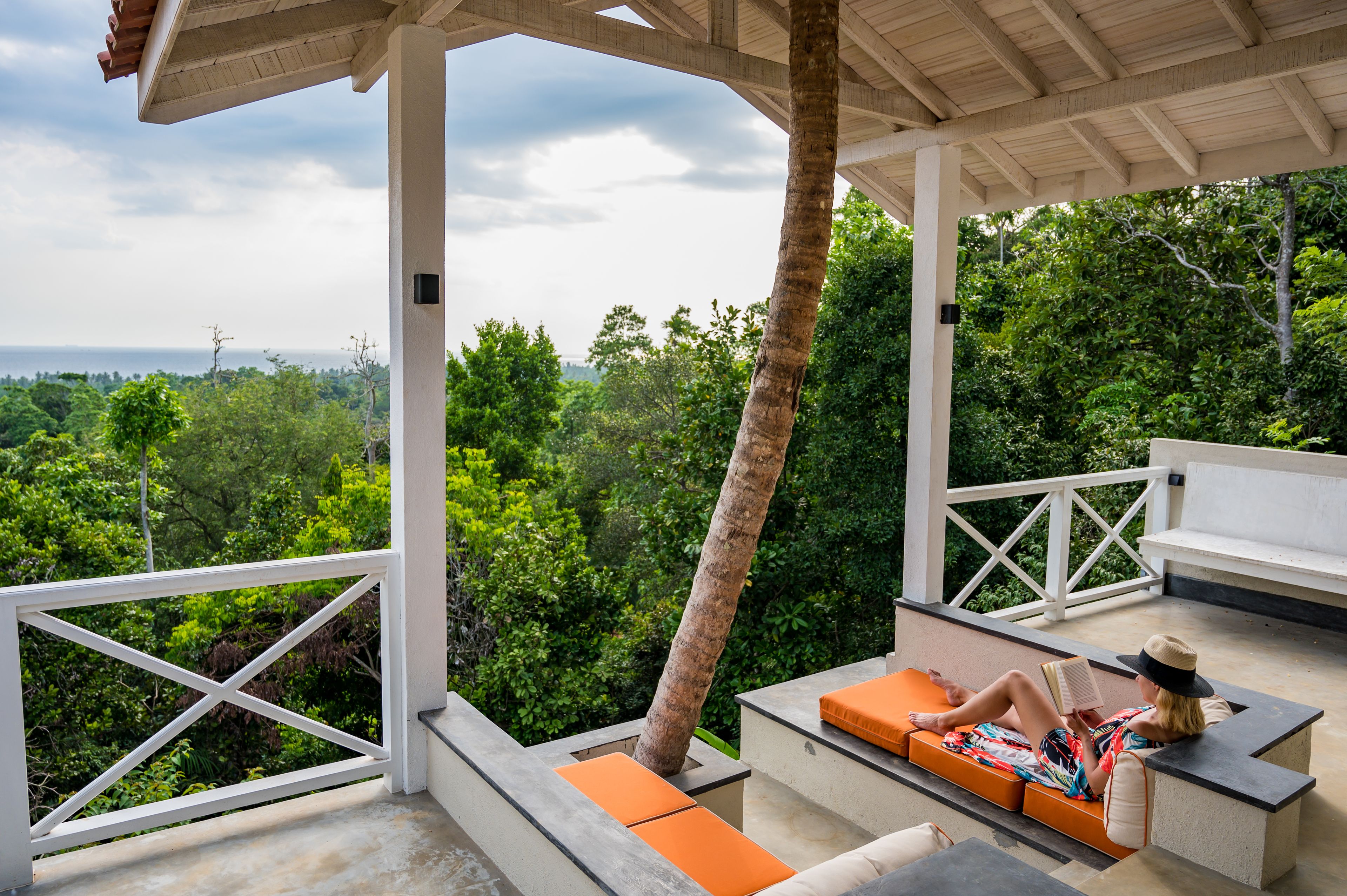 A covered outdoor seating area with a view of lush greenery and the sea.