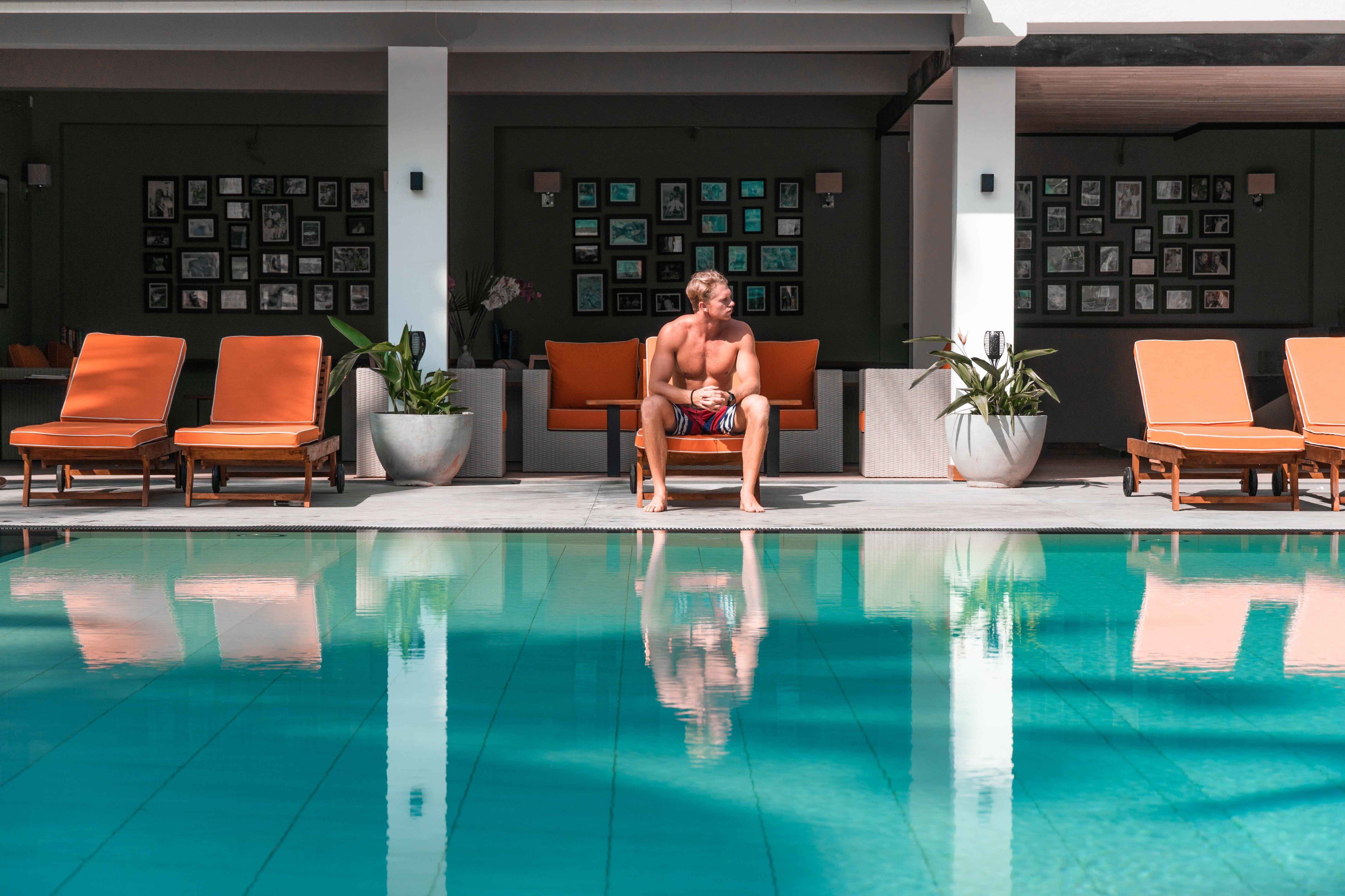 A poolside area with orange lounge chairs, a pool, and framed pictures on the walls.