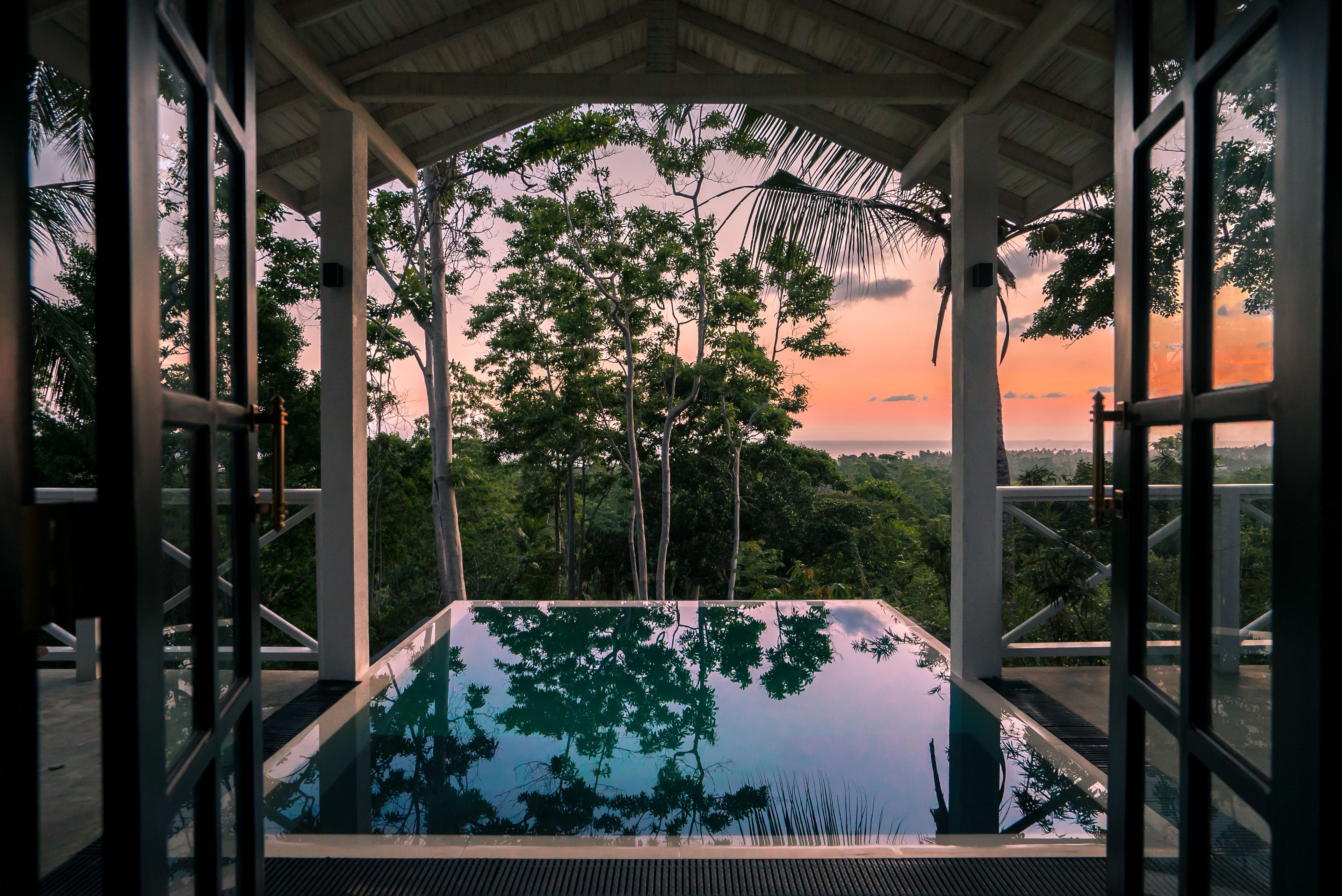 Una piscina infinita con vistas a árboles y un atardecer.