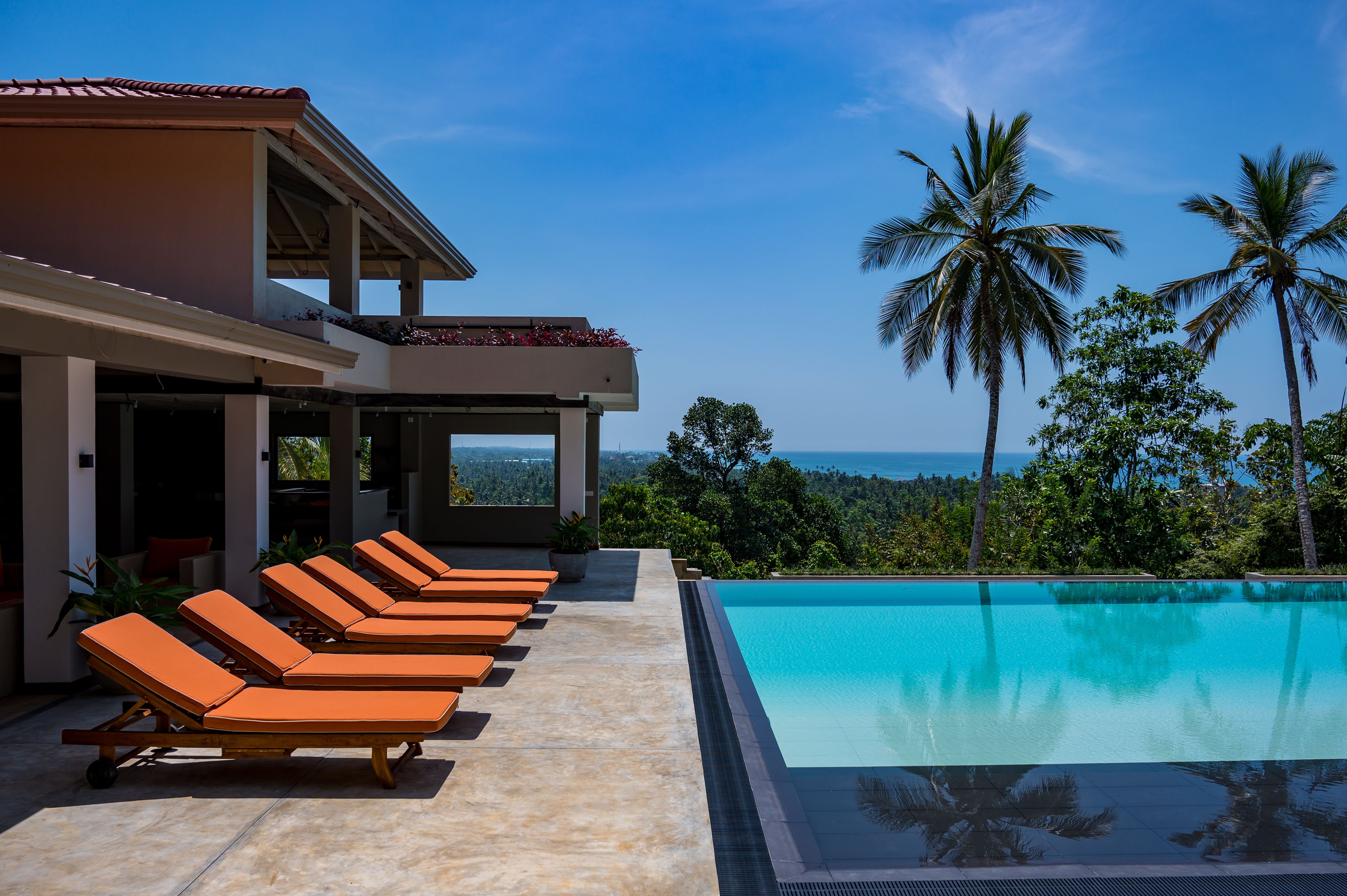 A poolside area with lounge chairs, a clear blue pool, and a view of the ocean.