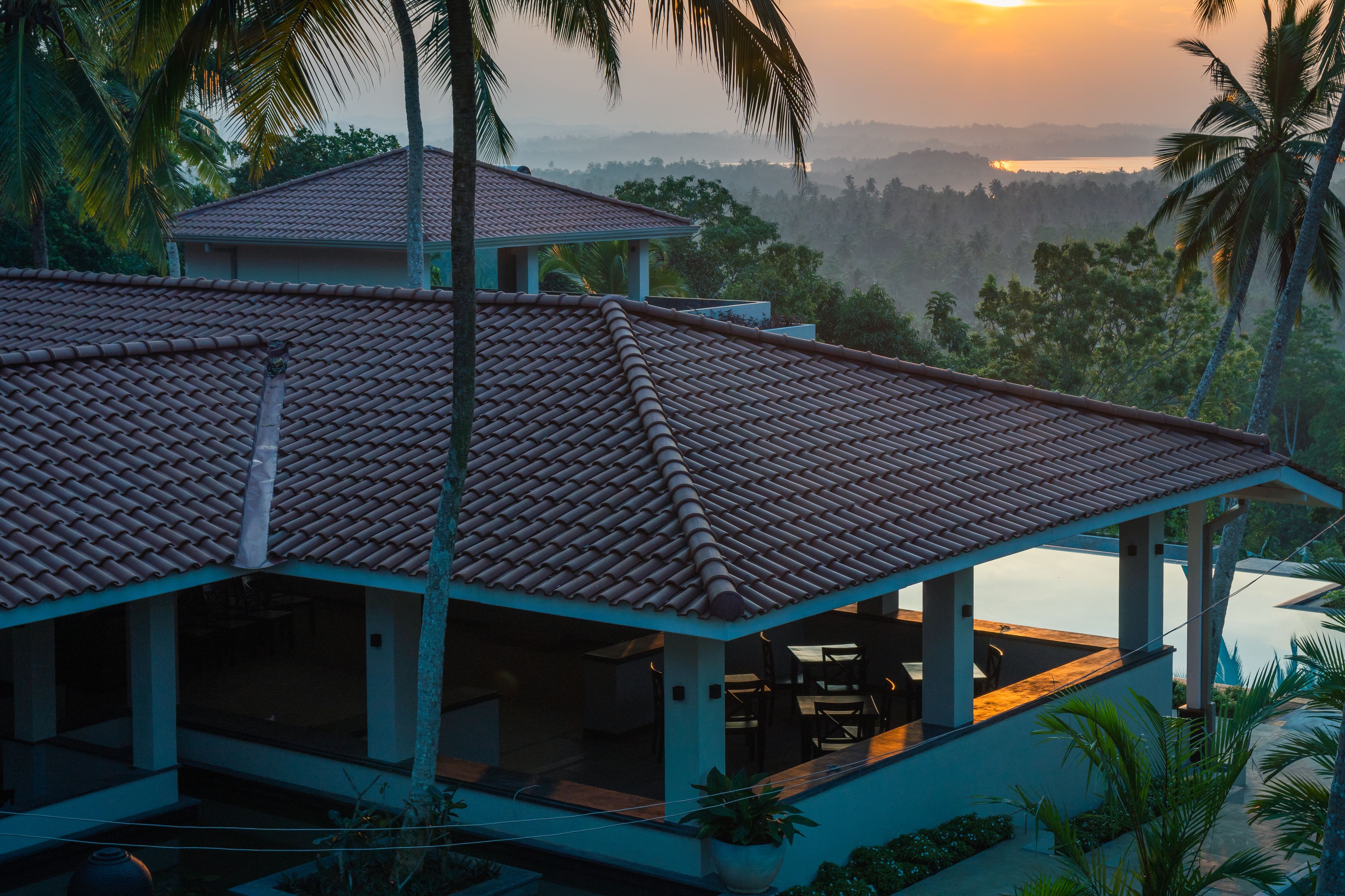 A house with a tiled roof, a covered patio, and a view of a lake and forest.