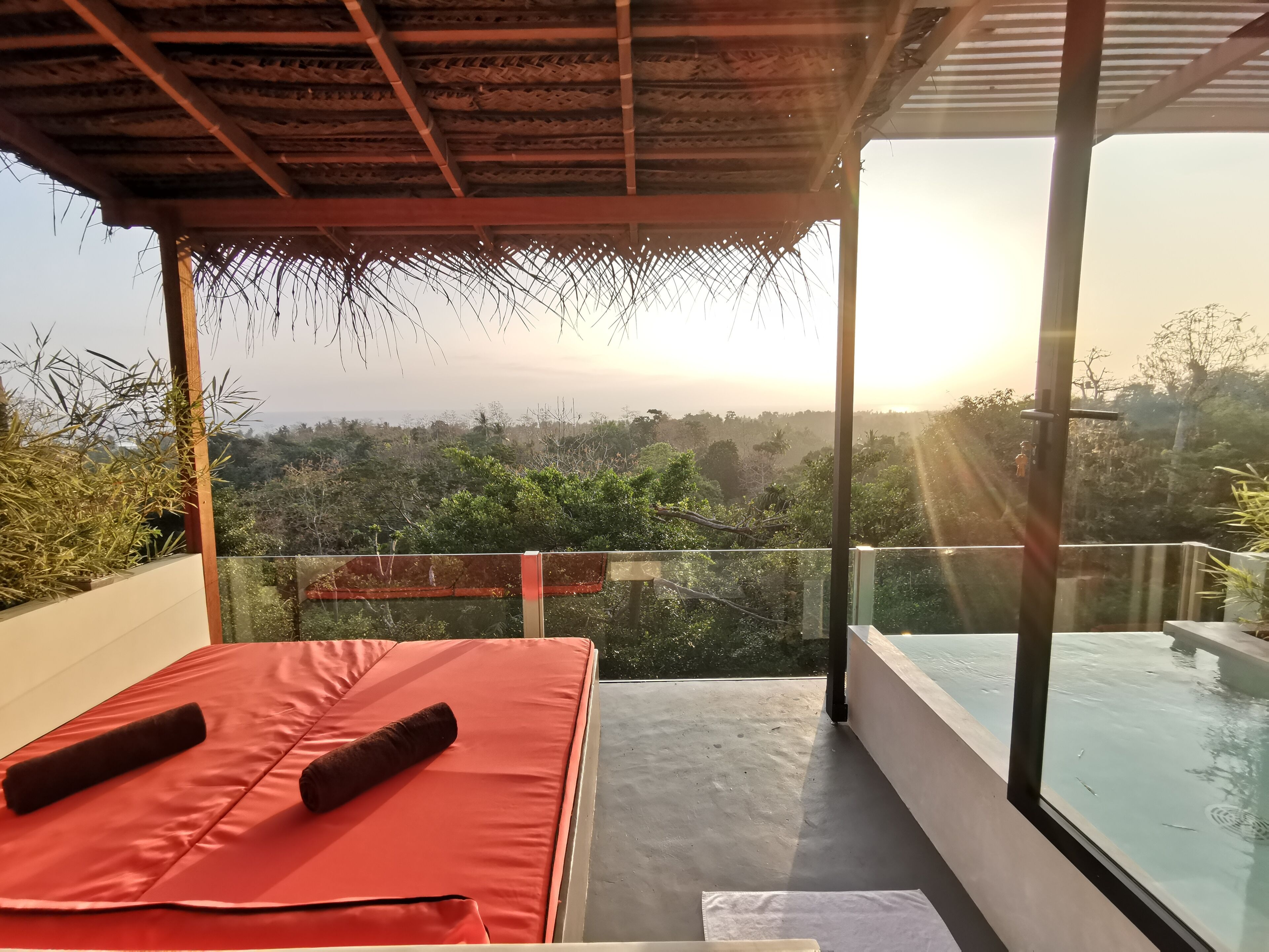 A balcony with a red mat and two rolled-up towels, overlooking a lush landscape with a clear view of the horizon.