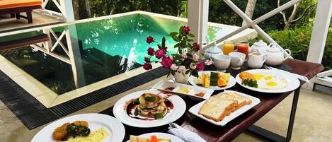 Una mesa de desayuno con diversos platos y vistas a una piscina.
