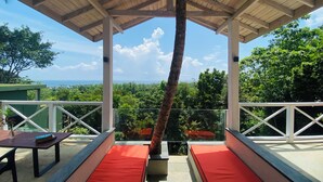 Un espacio de estar al aire libre cubierto con cojines rojos, techo de madera y vistas al océano y la vegetación.