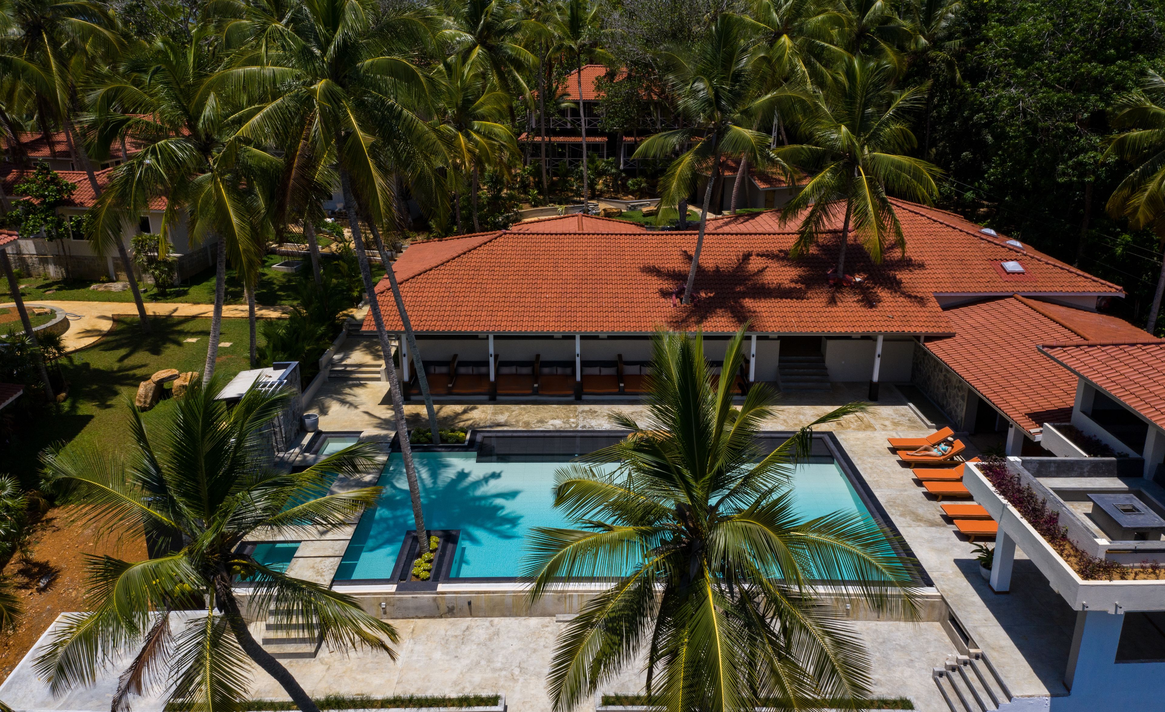 A resort with a swimming pool, palm trees, and a red-roofed building.
