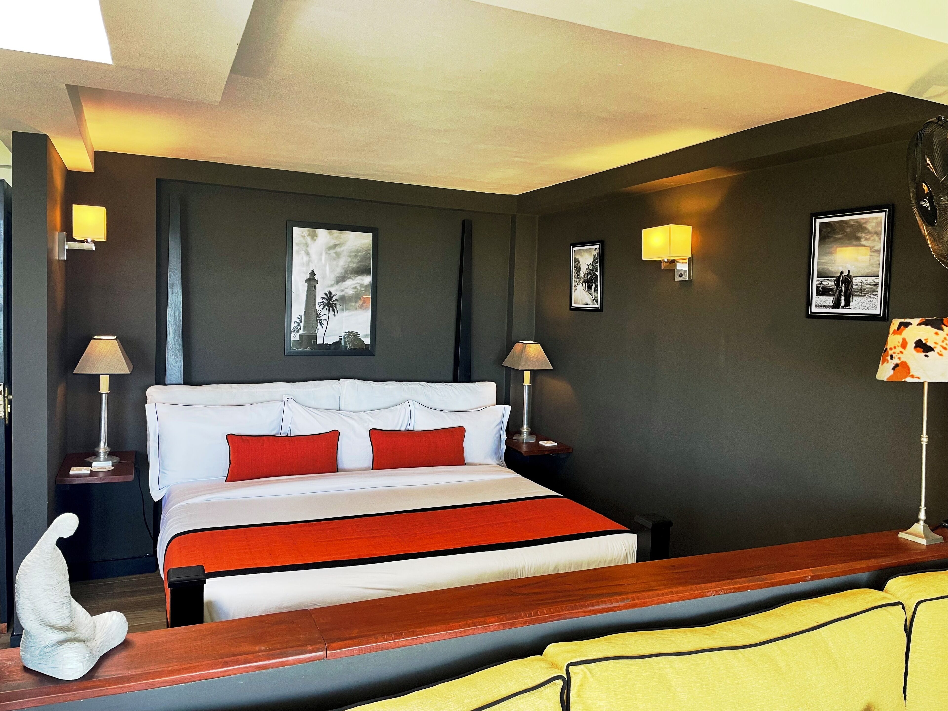 A hotel room with a large bed, two bedside tables with lamps, dark walls, and framed pictures on the walls.