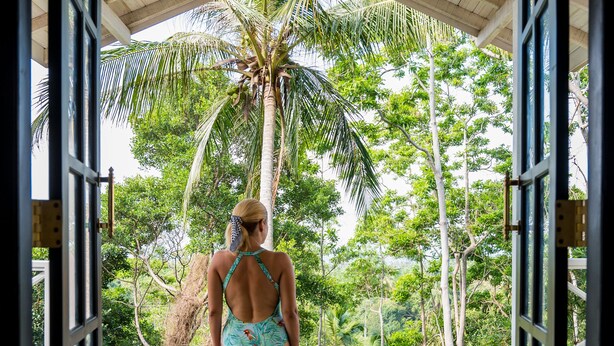 Una persona parada al borde de una piscina, con vistas a palmeras y un paisaje natural.