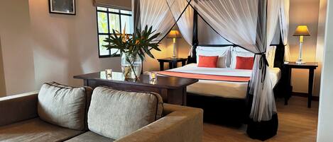 A hotel room with a bed, a sofa, a nightstand, a lamp, and a window.