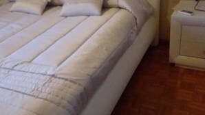 A bed with a white headboard and multiple pillows, a bedside table with a lamp, and a wooden floor. - Agrigento Templi Pool Garden (Camastra)