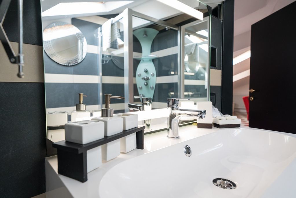 Ein modernes Badezimmer mit einem großen, weißen Waschbecken, zwei Spiegeln und einer dekorativen Vase.
