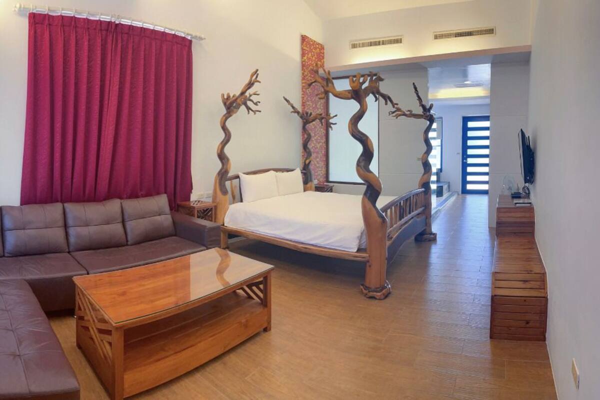A bedroom with a wooden four-poster bed, a sofa, and a wooden coffee table.