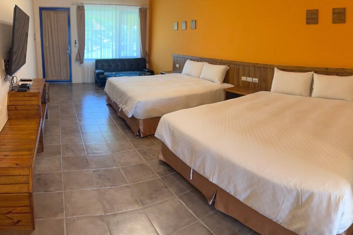 A hotel room with two beds, a TV, a desk, and a window with curtains.