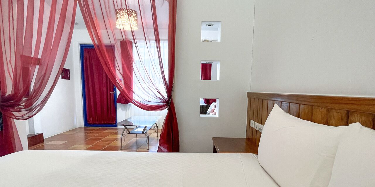 Une chambre à coucher avec un lit, une table de chevet, une tête de lit en bois, un rideau rouge et une petite table avec une chaise.