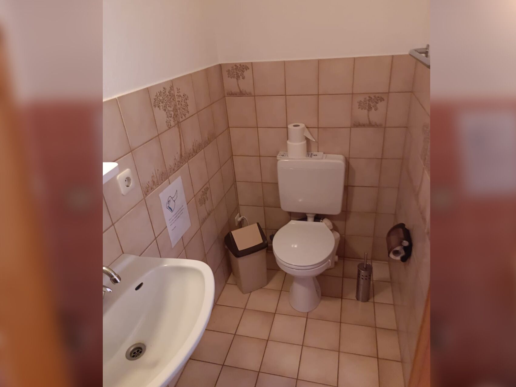 Et lille badeværelse med toilet, håndvask og skraldespand.