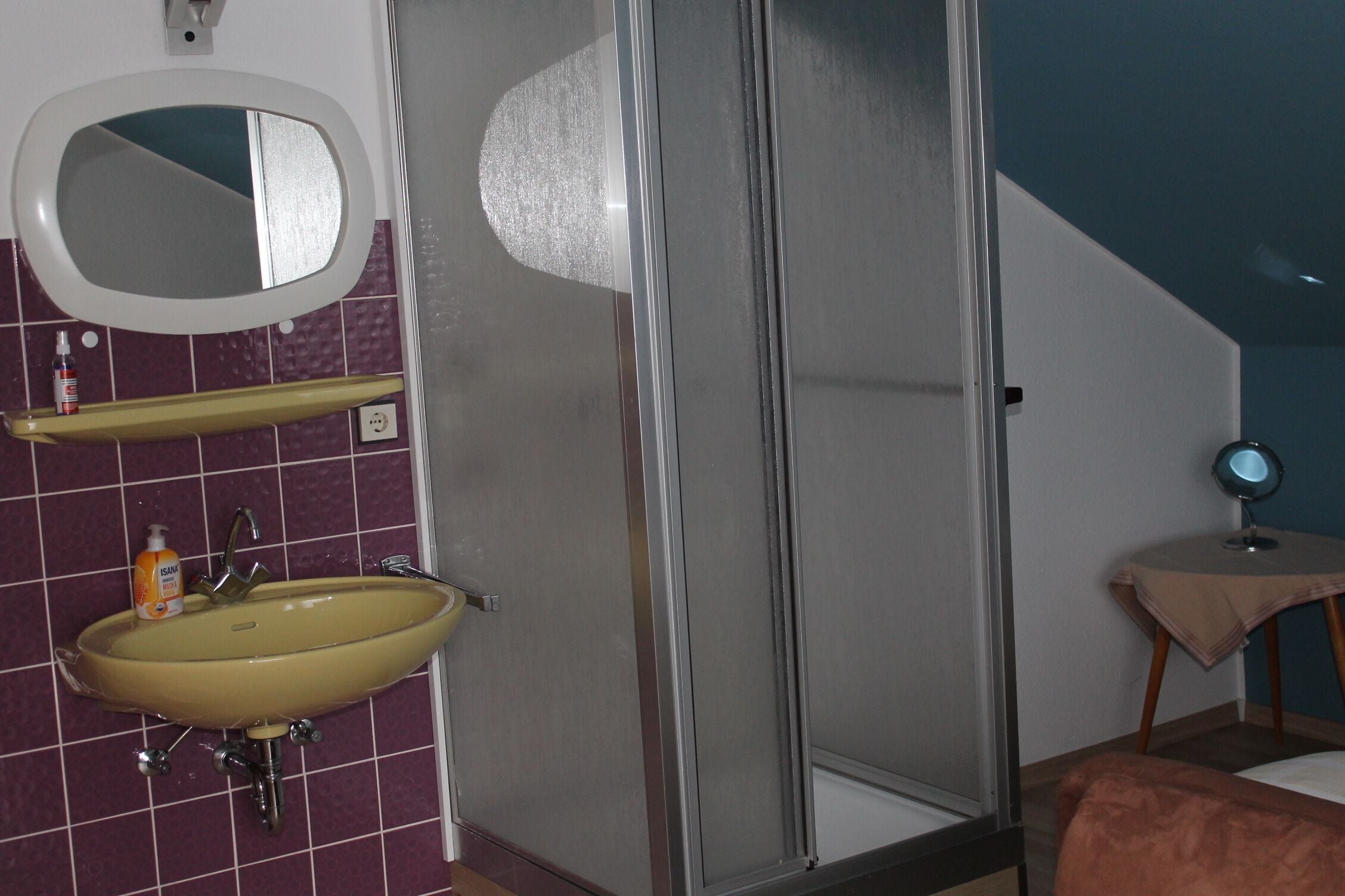 A bathroom with a yellow sink, a mirror, a shower, and a small table with a round mirror.