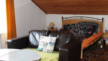 Una habitación con cama, sofá de cuero, una mesita y una lámpara.