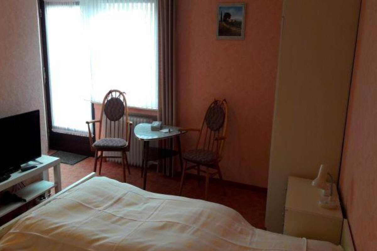 A hotel room with a bed, a television, a small table with two chairs, and a window with curtains.