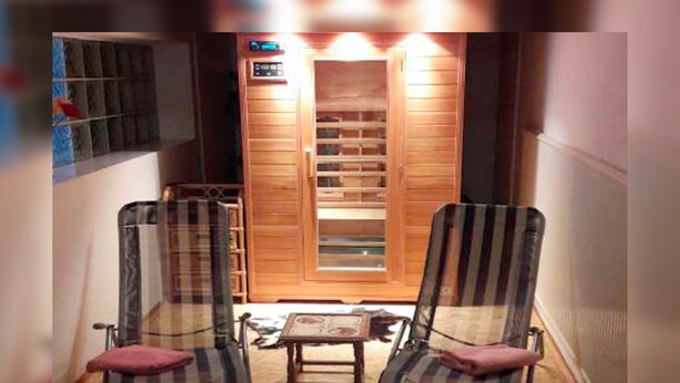 A sauna room with two striped chairs, a small table, and a wooden door with a control panel. - Hotel Haus Erlen (Olsberg)