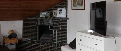 A room with a brick fireplace, a white dresser, a television, and a framed picture on the wall.