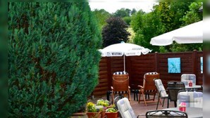 An outdoor seating area with wooden chairs and tables, a white umbrella, and potted plants. - Hotel Haus Erlen (Olsberg)