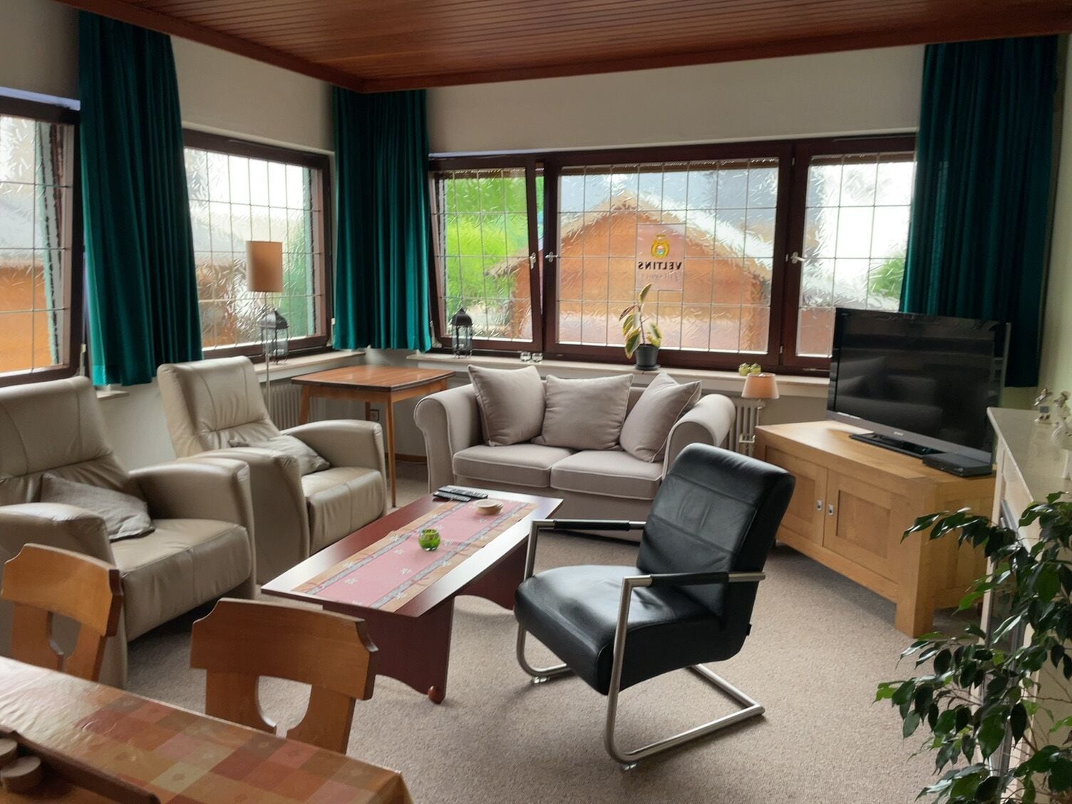 Un salón amplio con un conjunto de sofás, una mesa de comedor, un televisor y ventanas grandes con cortinas.