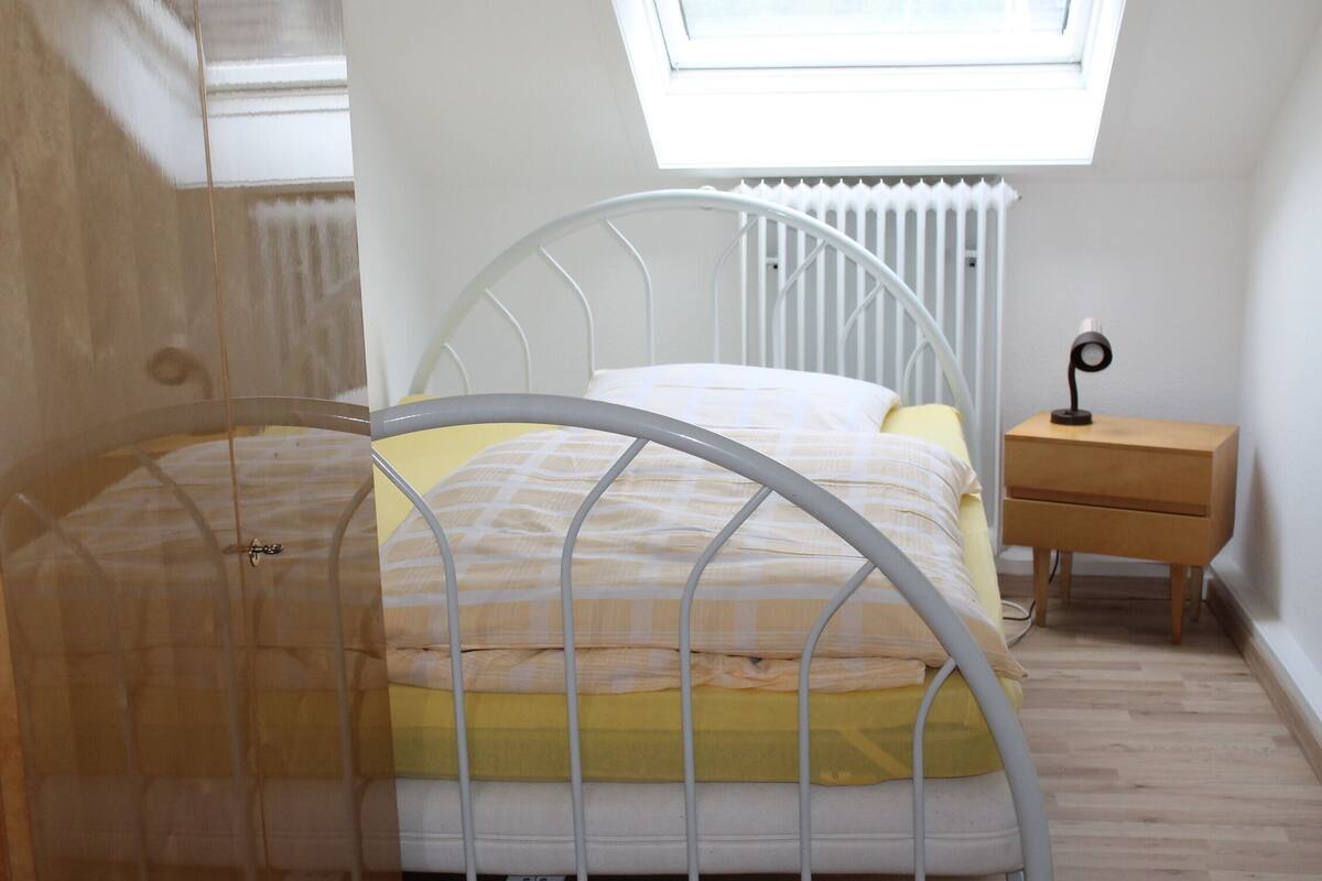 A bedroom with a metal bed frame, a bedside table, a radiator, and a skylight.