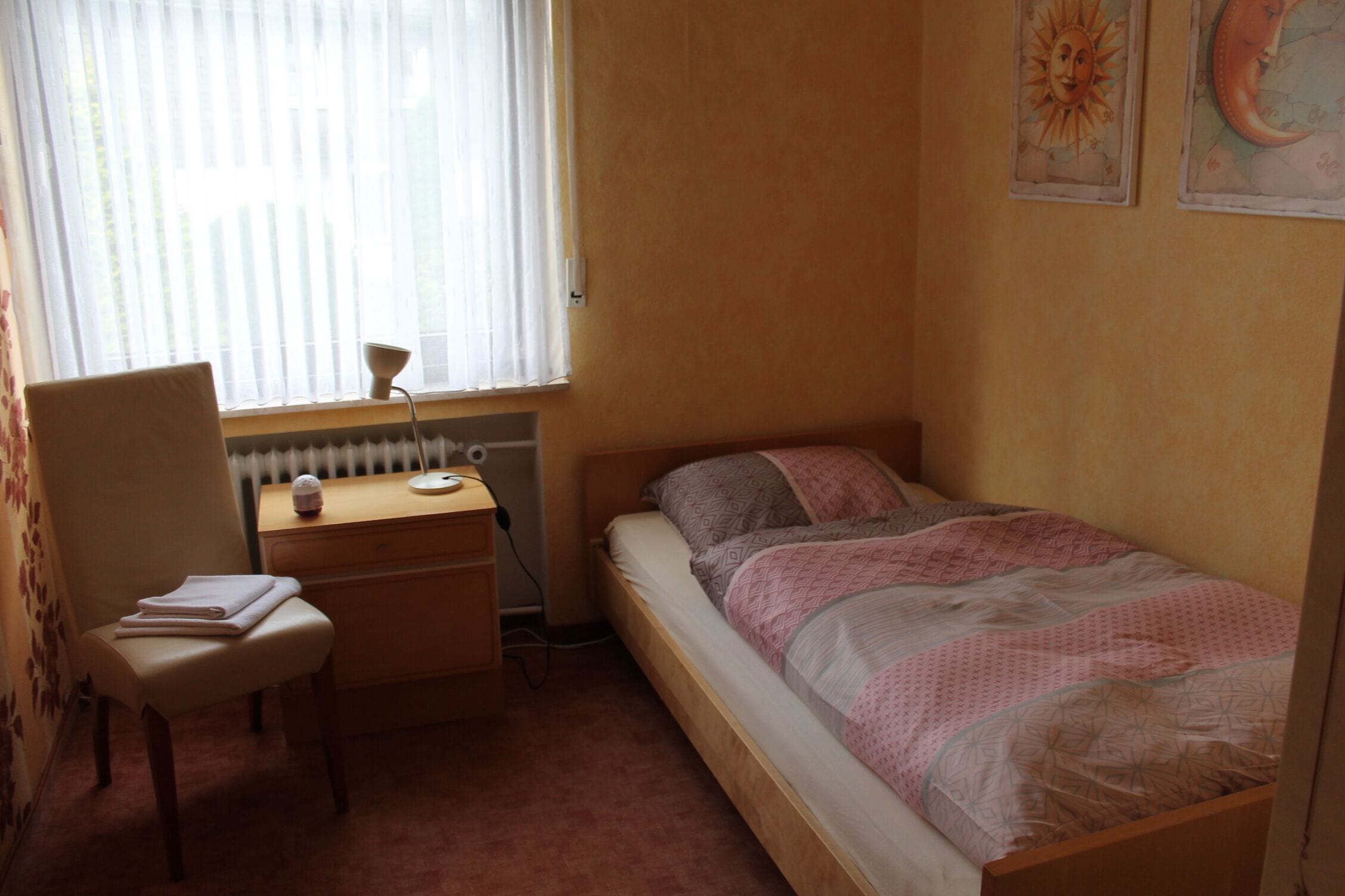 Una camera da letto con un letto singolo, una scrivania con una sedia, un termosifone e una finestra con persiane.