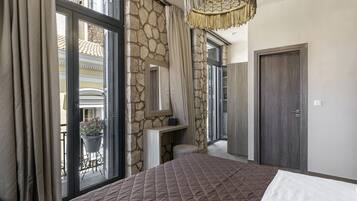 A bedroom with a large bed, stone walls, a chandelier, and a view of the outside balcony.
