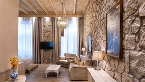 A spacious living room with a stone wall, a flat-screen TV, a sofa, a coffee table, and a lamp. - Athens Manor Houses Suites Apartments (Athens)