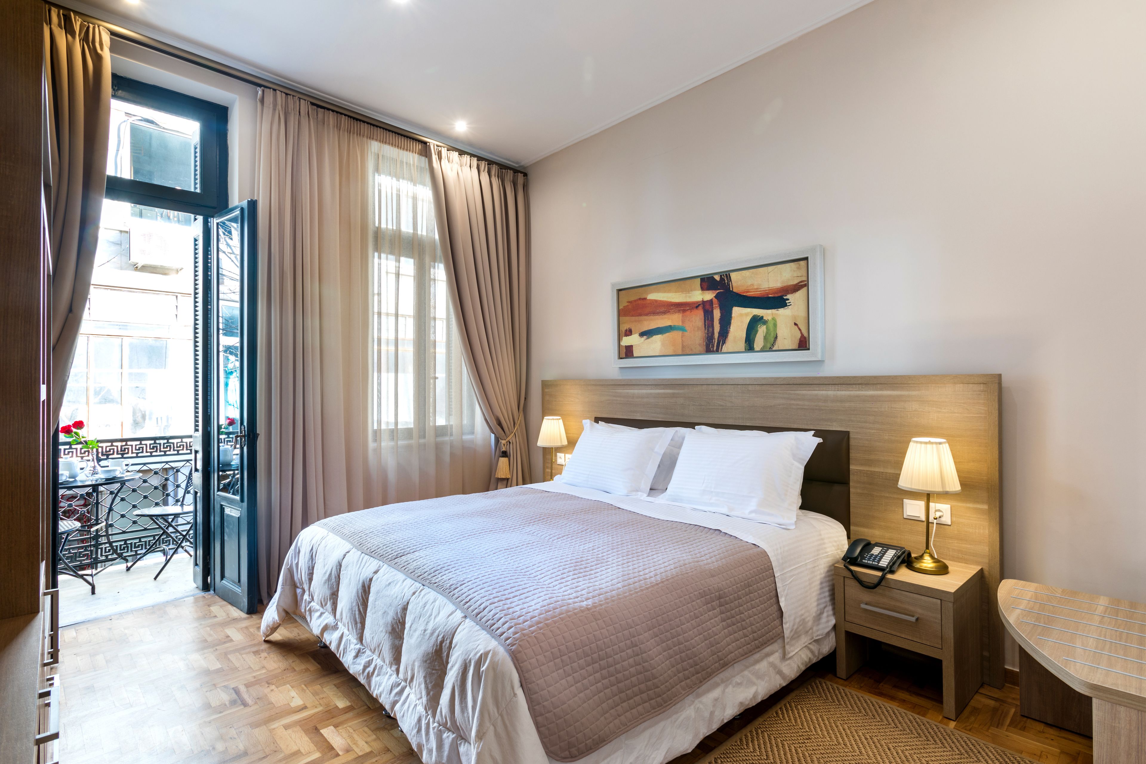 A hotel room with a bed, bedside lamps, a painting on the wall, and a view of the outside balcony.
