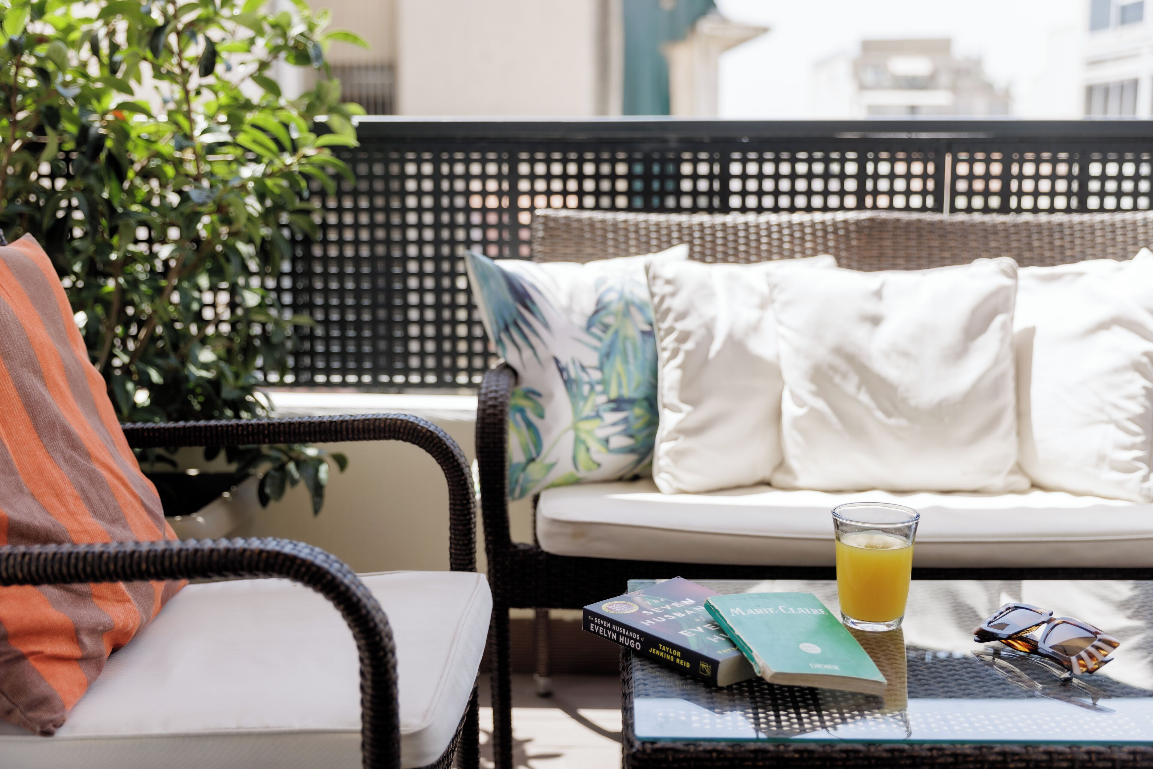 A wicker sofa with white cushions, a glass of orange juice, and a book on a table.