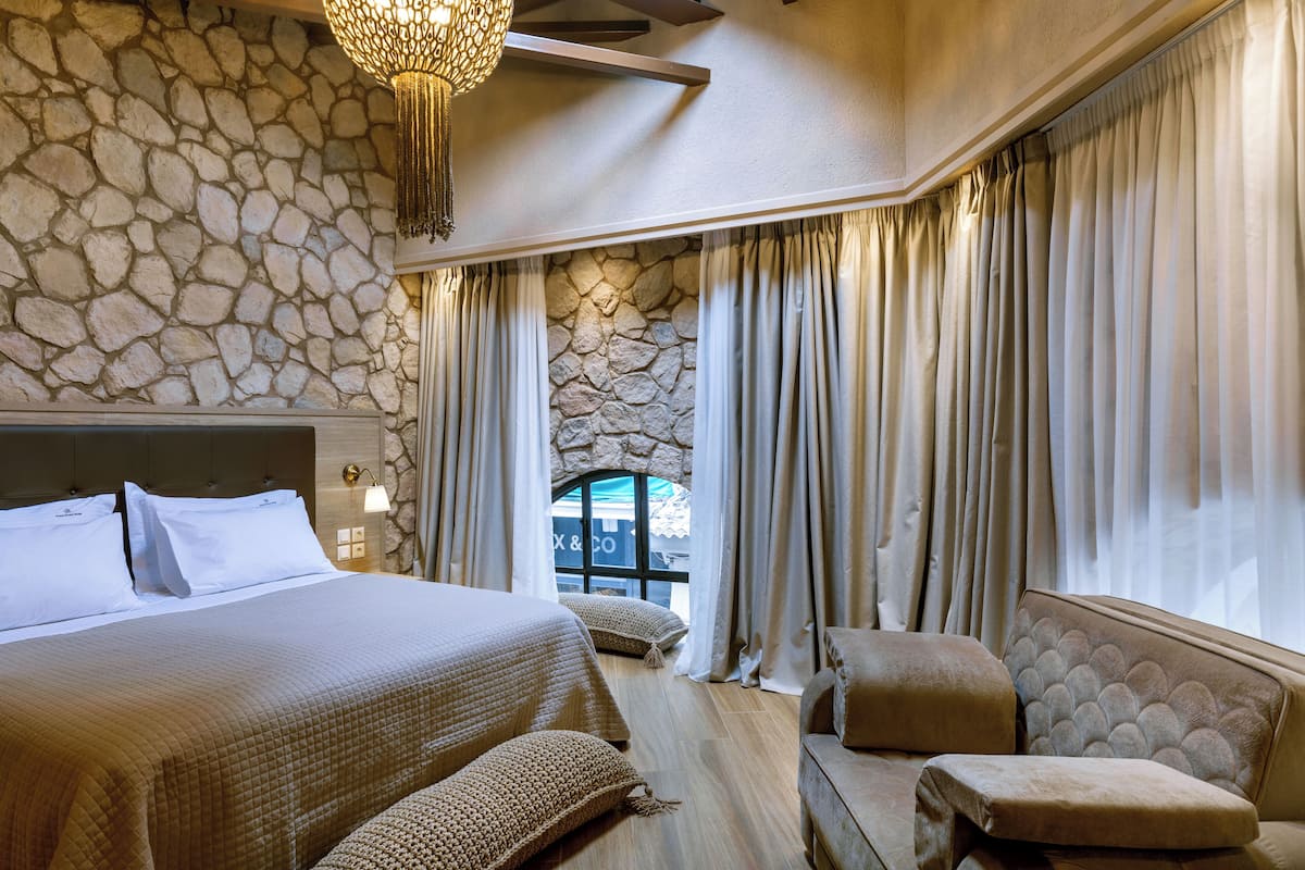 Une chambre avec un mur en pierre, un grand lit, un canapé et une vue sur l’extérieur.