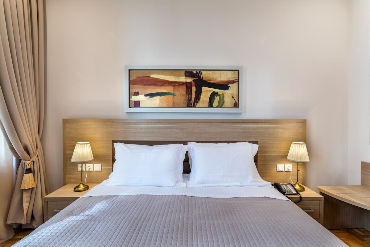 Une chambre d’hôtel avec un grand lit, deux tables de chevet avec des lampes, une tête de lit en bois et un tableau au-dessus du lit.