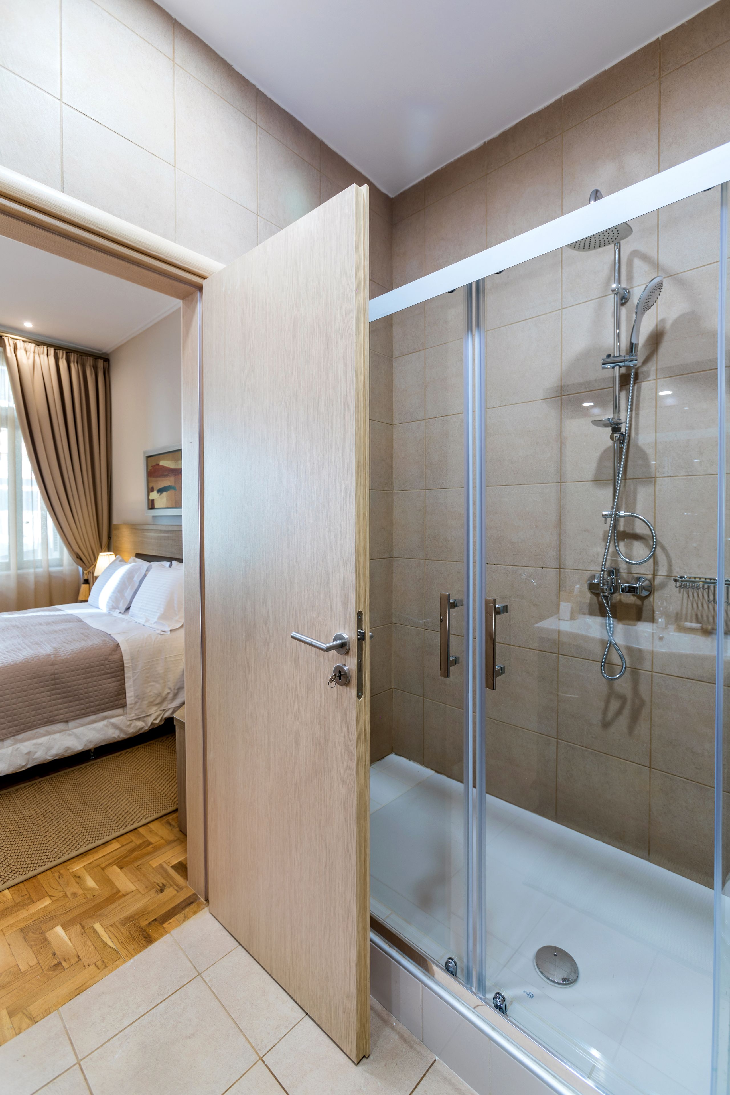 Ein Hotelzimmer mit einer gläsernen Duschkabine, einem Bett mit Kopfteil und Holzboden.