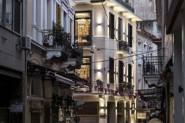 Una calle estrecha con edificios de varios pisos, balcones con plantas e iluminación colgante.